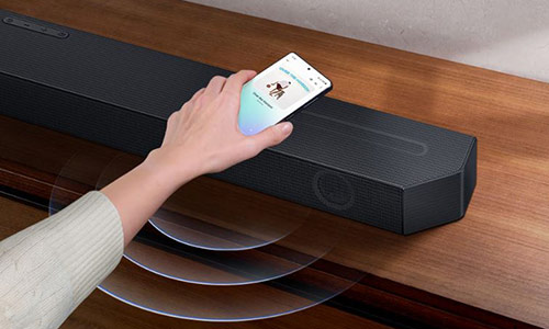A hand taps a smartphone with the Samsung music app on-screen on the Soundbar. It instantly plays music, showing how easy it is to switch from smartphone to Soundbar