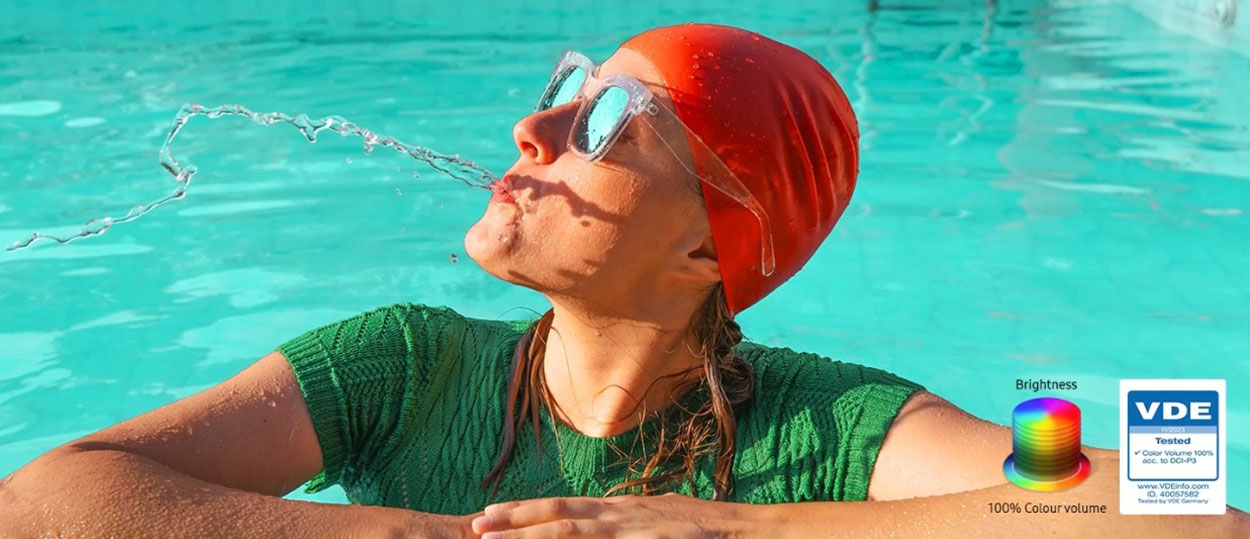 A woman is spitting out water in the pool. All the colors in the image become vivid as the brightness level increases. VDE tested logo is on display.