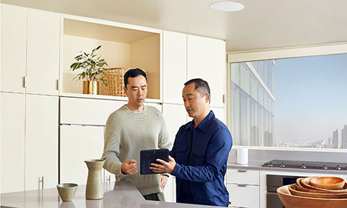 Two men chatting in the kitchen with Sonance in-ceiling speakers installed above a kitchen island