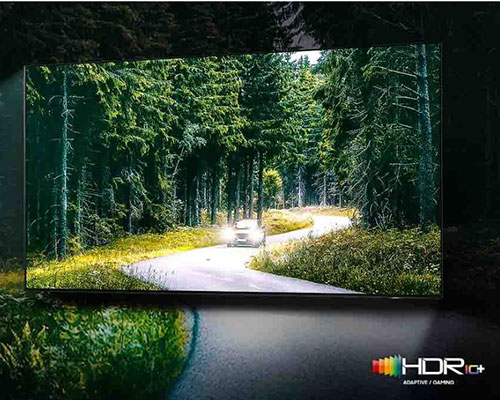 A car is running with lights on through a forest. There is a comparison between SDR and HDR 10+ quality in terms of brightness and intensity.