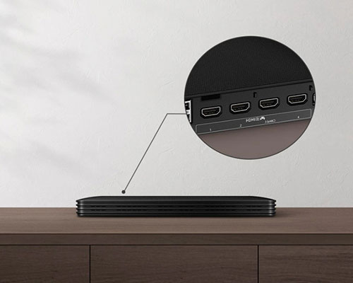 The One Connect Box is on a table. Its various ports on the back are zoomed in. The Attachable One Connect Box is attached to the back of the OLED TV to minimize clutter.