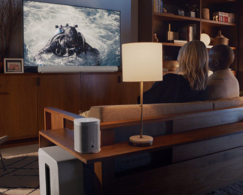Couple watching TV with white Sonos Arc home theatre system